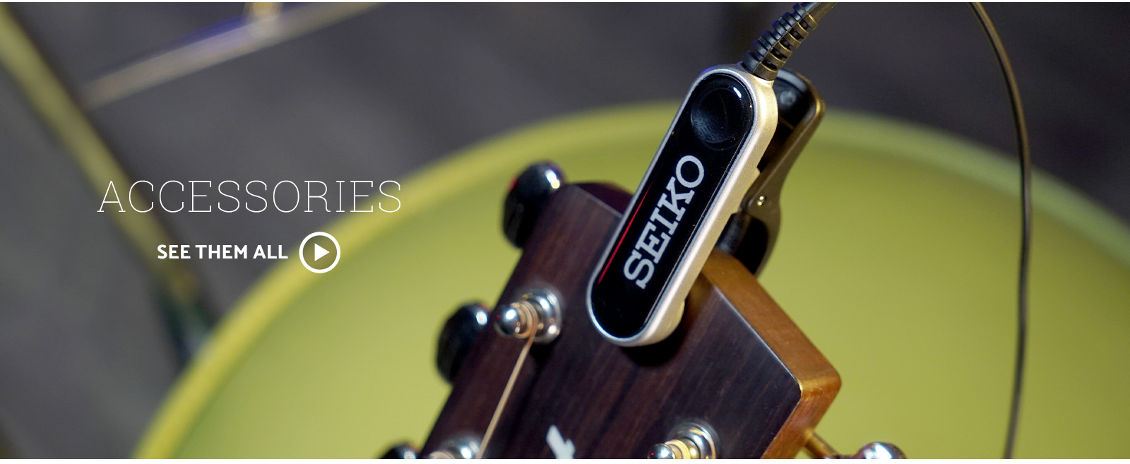Seiko clip on microphone is clipped to an acoustic guitar headstock in front of a green stool. Text says Accessories, click to see them.
